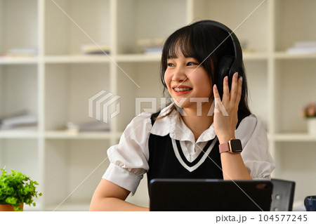 Pretty teenage asian woman listening music in wireless headphones and looking away. People, technology and lifestyle concept 104577245
