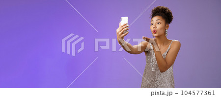 Charming elegant young female student partying enjoying prom recording video smartphone look phone display send air kiss blowing mwah taking selfie hold gadget, standing blue background Charming elegant young female student partying enjoying prom recording video smartphone look phone display send air kiss blowing mwah taking selfie hold gadget, standing blue background 104577361