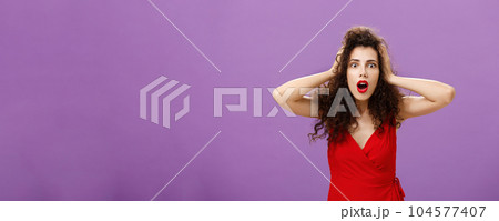 You do not say. Portrait of shocked and impressed speechless woman with curly haircut in luxurious evening dress opening mouth from amazement and shock holding hands on head stunned over puple wall 104577407