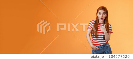 Outgoing good-looking redhead modern girl wonder making amazing purchase, look camera surprised, questioned pointing left, interested about new cool promo, stand orange background 104577526