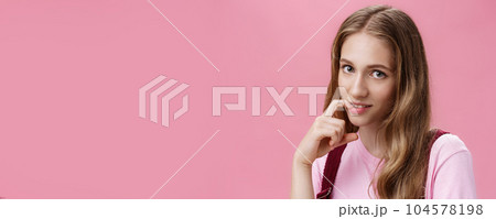 Cute feminine girl learning how make glances and seduce boyfriend with flirty gaze biting finger sensually posing against pink background, flirting making senducing look wearing make-up on date 104578198