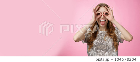Carefree playful funny young party girl fool around showing tongue immature mimicking make goggles from hands widen eyes look through circles, having fun entertain friends, standing pink background Carefree playful funny young party girl fool around showing tongue immature mimicking make goggles from hands widen eyes look through circles, having fun entertain friends, standing pink background 104578204