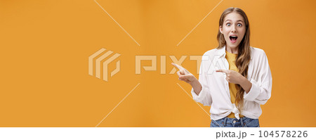 Waist-up shot of excited speechless impressed young cute woman with curly hair dropping jaw from amazement pointing left thrilled telling about awesome copy space at camera astonished Waist-up shot of excited speechless impressed young cute woman with curly hair dropping jaw from amazement pointing left thrilled telling about awesome copy space at camera astonished 104578226