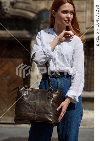 photo of a woman wearing blue jeans and white blouse with a brown leather handbag . 104578290