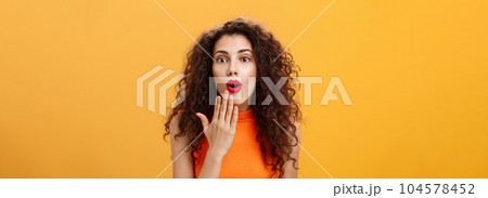 Waist-up shot of amazed and excited caucasian woman with curly hair in red lipstic opening mouth from surprise covering it with palm listening shocking rumors reacting astonished to amusing news 104578452