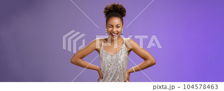 Cheeky good-looking african-american woman in silver glittering dress hold hand waist show tongue daring winking camera feel lucky standing thrilled dancing have fun partying, blue background 104578463