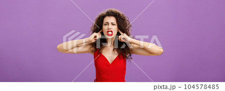 Woman fed up of hearing cursing words and arguments in her turn. Portrait of displeased insecure and offended female with curly hairstyle in red dress closing eyes and talking displeased and bothered 104578485