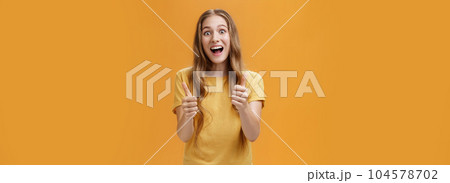 Excited girl expressed support and cheer raising thumbs up in approval and like gesture smiling optimistic and positive being amused with awesome idea standing pleased over orange background 104578702
