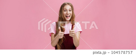 Friendly and outgoing pretty young woman in overalls with wavy natural hairstyle showing thumbs up gesture with cheer and joy smiling being supportive, liking idea, expressing positive opinion Friendly and outgoing pretty young woman in overalls with wavy natural hairstyle showing thumbs up gesture with cheer and joy smiling being supportive, liking idea, expressing positive opinion 104578757