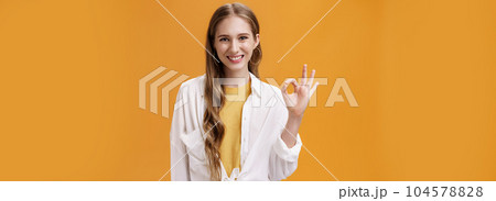 It is okay. Friendly-looking pleasant smiling girl with wavy hair in trendy blouse over t-shirt showing ok or perfect gesture smiling assertive and assured giving positive answer over orange wall It is okay. Friendly-looking pleasant smiling girl with wavy hair in trendy blouse over t-shirt showing ok or perfect gesture smiling assertive and assured giving positive answer over orange wall 104578828