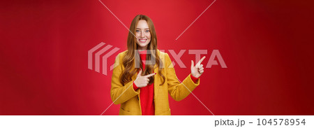 Cheerful friendly-looking and energized helpful redhead girl in yellow coat showing way pointing at upper left corner and smiling broadly with satisfied grin posing delighted over red background Cheerful friendly-looking and energized helpful redhead girl in yellow coat showing way pointing at upper left corner and smiling broadly with satisfied grin posing delighted over red background 104578954