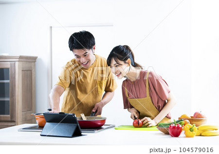 タブレットを見ながら料理をする若い夫婦 104579016