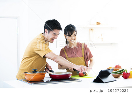 タブレットを見ながら料理をする若い夫婦 104579025