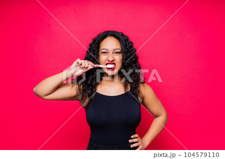Happy African American woman brushes teeth. Dental hygiene concept. Isolated on red background. 104579110