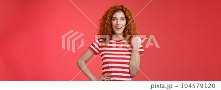 Sassy good-looking emotive happy smiling redhead european female curly hairstyle pointing thumb left grin assertive cheeky hold hand waist directing promo advertising offer red background Sassy good-looking emotive happy smiling redhead european female curly hairstyle pointing thumb left grin assertive cheeky hold hand waist directing promo advertising offer red background 104579120