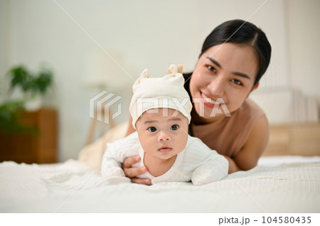 Sweet family moment. Young Asian mom lay down with her baby, smiling to camera. 104580435