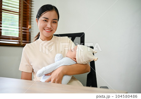 Young beautiful Asian mother working at home and holding her baby in her arms. 104580486