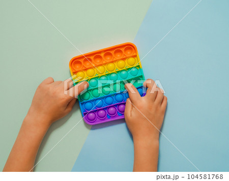 Kid hands play with popit toy over blue background Kid hands play with popit toy over blue background 104581768
