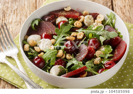 Vegetarian salad of arugula, beets, ripe cherries, cheese, hazelnuts close-up in a bowl. Horizontal Vegetarian salad of arugula, beets, ripe cherries, cheese, hazelnuts close-up in a bowl. Horizontal 104585098