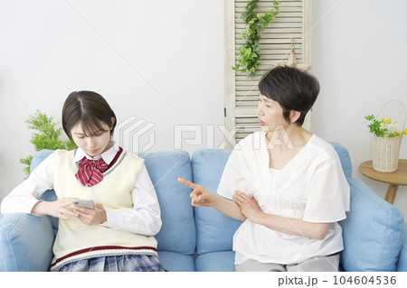 自宅で母親の前でスマートフォンを使う女子高生 104604536