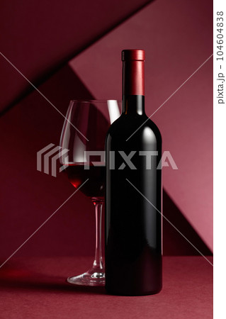 Bottle and glass of red wine on a red background. Bottle and glass of red wine on a red background. 104604838