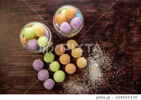Portioned colored sugar scrubs balls folded into a glass jar and neatly laid out on a wooden table. 104605330