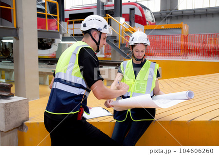Young caucasian engineer man and woman or worker looking blueprint and checking electric train. 104606260
