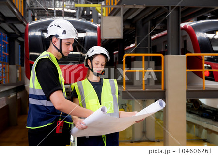 Young caucasian engineer man and woman or worker looking blueprint and checking electric train. Young caucasian engineer man and woman or worker looking blueprint and checking electric train. 104606261