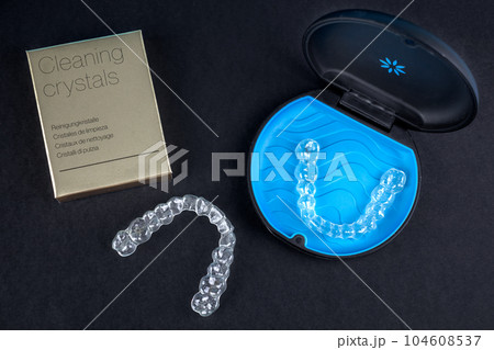 Invisible retainers case with orthodontic aligner brackets top view. Black plastic dental container for invisalign braces and cleaning crystals for them. Invisible retainers case with orthodontic aligner brackets top view. Black plastic dental container for invisalign braces and cleaning crystals for them. 104608537