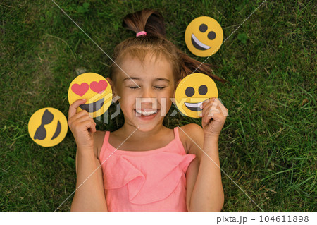 Cute hilarious girl laughs merrily with her eyes closed holding various emoticons with different emotions in hands 104611898
