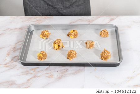 Scooping cookie dough into the baking sheet lined with parchment paper to bake apple oatmeal cookies. Scooping cookie dough into the baking sheet lined with parchment paper to bake apple oatmeal cookies. 104612122