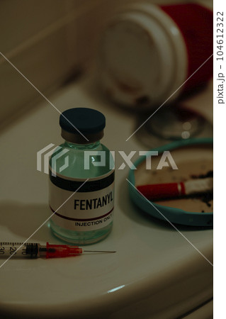 syringe and simulated vial of fentanyl on a toilet 104612322