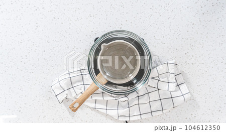 Flat lay. Melting chocolate chips and other ingredients in a glass mixing bowl over boiling water to prepare plain fudge. Flat lay. Melting chocolate chips and other ingredients in a glass mixing bowl over boiling water to prepare plain fudge. 104612350