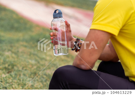 The athlete, taking a break, rests at the sports arena, holding his water bottle,  104613229