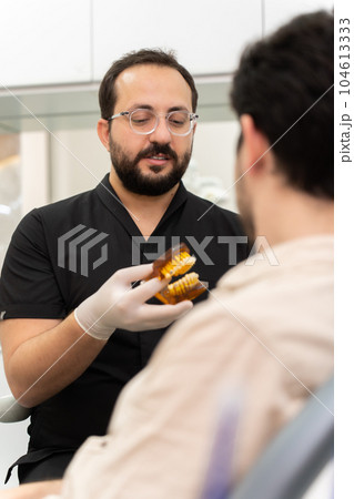 Doctor in black uniform recommending patient to install dental braces and solve orthodontic problems consulting man during regular teeth examination in clinic Doctor in black uniform recommending patient to install dental braces and solve orthodontic problems consulting man during regular teeth examination in clinic 104613333