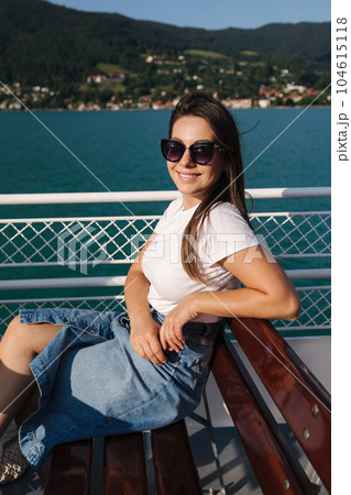 Attractive young woman sitting on bench during the excursion along the lake on ship 104615118