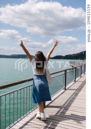 Back view of woman raised her hands up. Female walking through the embankment. Emotion of beauty of nature. Clear water. Back view of woman raised her hands up. Female walking through the embankment. Emotion of beauty of nature. Clear water. 104615134