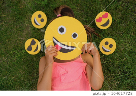 A woman hides her face behind emojis making faces. A variety of emoticons reflecting the emotional state A woman hides her face behind emojis making faces. A variety of emoticons reflecting the emotional state 104617728