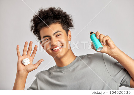 Young guy with black curly hair applies face wash to his hands, ready to take on his daily grooming and skincare routine. Man preparing for a good face wash, the foundation of fresh and healthy skin. Young guy with black curly hair applies face wash to his hands, ready to take on his daily grooming and skincare routine. Man preparing for a good face wash, the foundation of fresh and healthy skin. 104620539