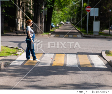 Blind pregnant woman crosses the road at a crosswalk with a cane. Blind pregnant woman crosses the road at a crosswalk with a cane. 104628657