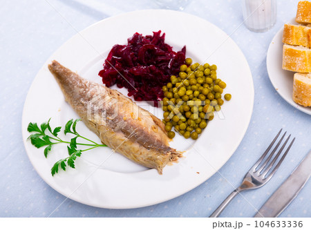 Slices herring fish with canned green peas, beetroot, decorated by mint served on plate with bread and cutlery 104633336