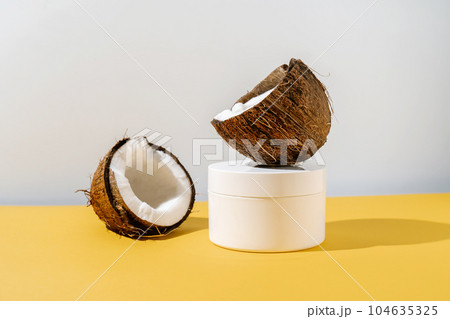 Two halves of coconut and a jar of cosmetics on a yellow and gray background. 104635325