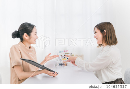 ネイルサロンでタブレットとネイルチップを見ながらネイリストにカウンセリングを受ける日本人女性 104635537