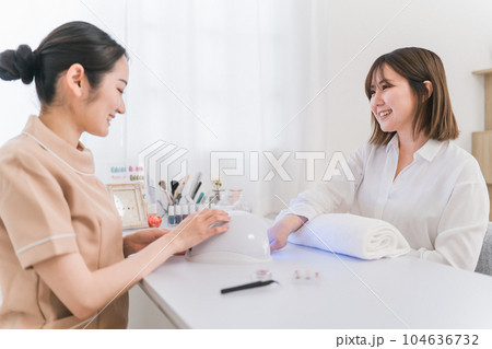 ネイルサロンでネイルをする女性とネイリスト（LEDライト・硬化） 104636732