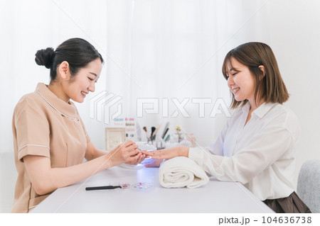 ネイルサロンでネイルをする女性とネイリスト(LEDライト・硬化) ネイルサロンでネイルをする女性とネイリスト(LEDライト・硬化) 104636738
