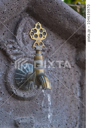 Water flows from an old copper faucet, a vertical shot of a sink in a public place on the street of the old city in Turkey, travel time, an idea for a background 104639970