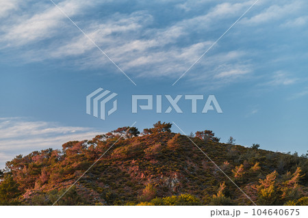 Scenic landscape of a hill against a sky of feather clouds in the red pink sunset light on the Aegean coast of Turkey, landscape or screensaver idea 104640675