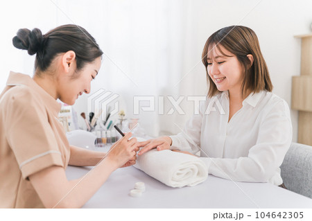 ネイルサロンでベースコートを塗るネイリストと女性 ネイルサロンでベースコートを塗るネイリストと女性 104642305