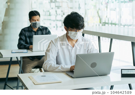 Asian colleague works while wearing a mask in the office during COVID-19. 104642589