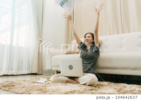 Asian woman throws papers in the living room as she finishes her work with her laptop on her lap. 104642637